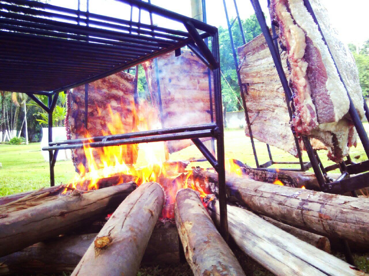 Costelão assando em estacas ao redor do fogo de chão, ao ar livre